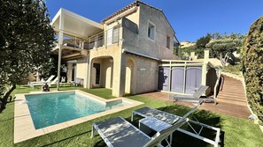 Una casa de dos pisos con piscina, mobiliario exterior y una escalera que conduce a un balcón.