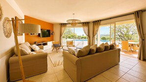 Una sala moderna con dos sofás, un televisor y un amplio ventanal con vistas a una piscina y follaje.