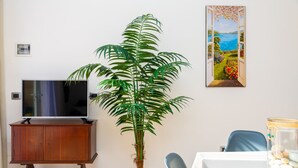 A room with a wooden cabinet, a large potted plant, a flat-screen TV, a dining table with a chair, and a framed painting on the wall. - APPARTAMENTO VICINO AL MARE - VICINO AL MARE (Portoferraio)
