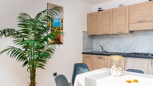 A modern kitchen with wooden cabinets, a black countertop, and a gas stove. There is a dining table with chairs and a large potted plant. - APPARTAMENTO VICINO AL MARE - VICINO AL MARE (Portoferraio)