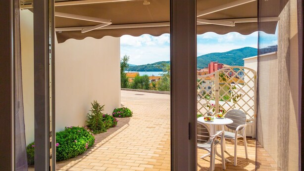 An outdoor patio with a table and chairs, a view of a lake, and buildings in the background. - APPARTAMENTO VICINO AL MARE - VICINO AL MARE (Portoferraio)
