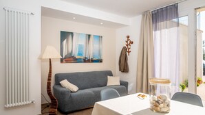 A modern living room with a grey sofa, a painting of sailboats, a lamp, and a table with a jar of pebbles. - APPARTAMENTO VICINO AL MARE - VICINO AL MARE (Portoferraio)