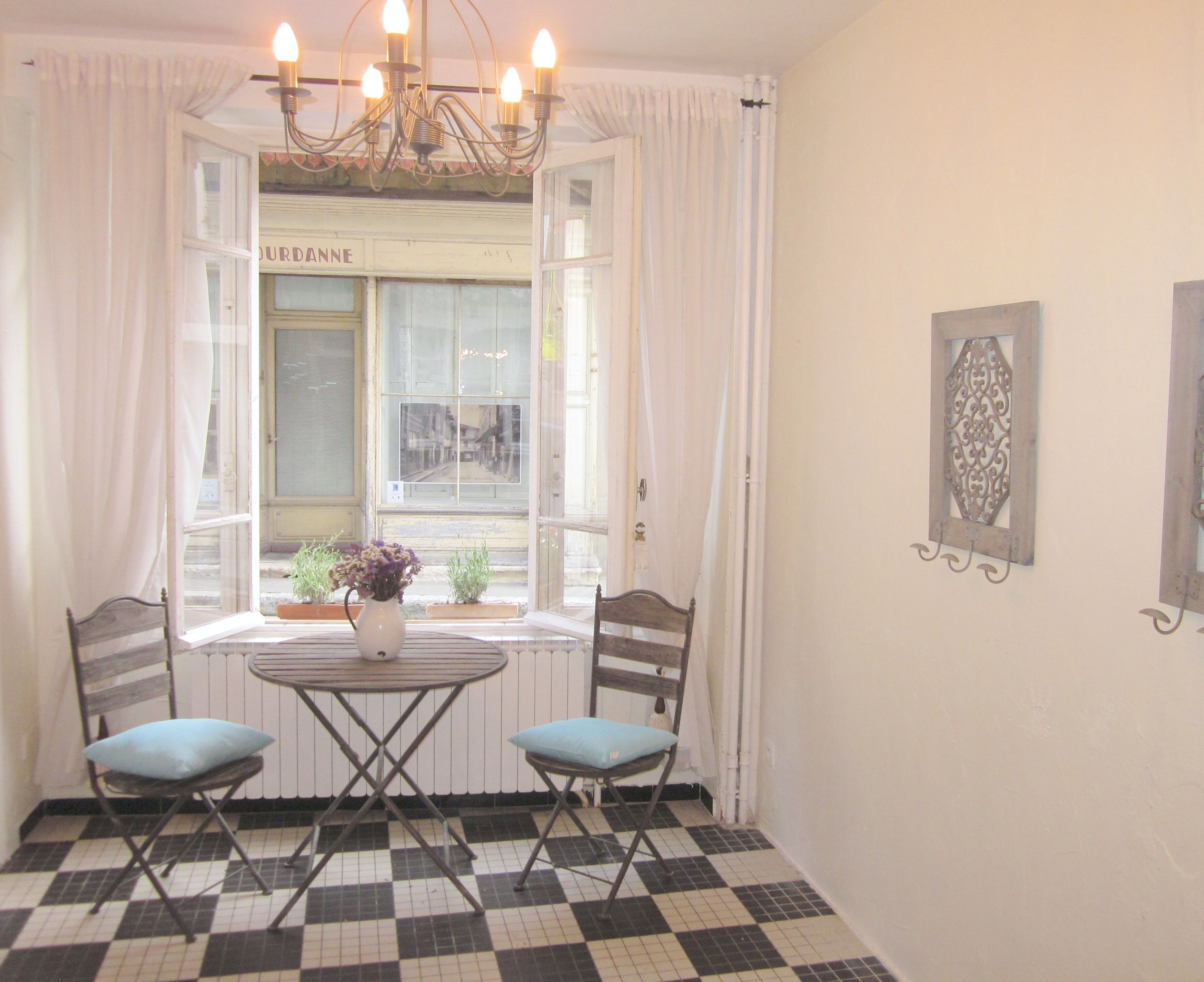 Une pièce avec un sol à carreaux, deux chaises, une table, un lustre et une fenêtre avec des rideaux.