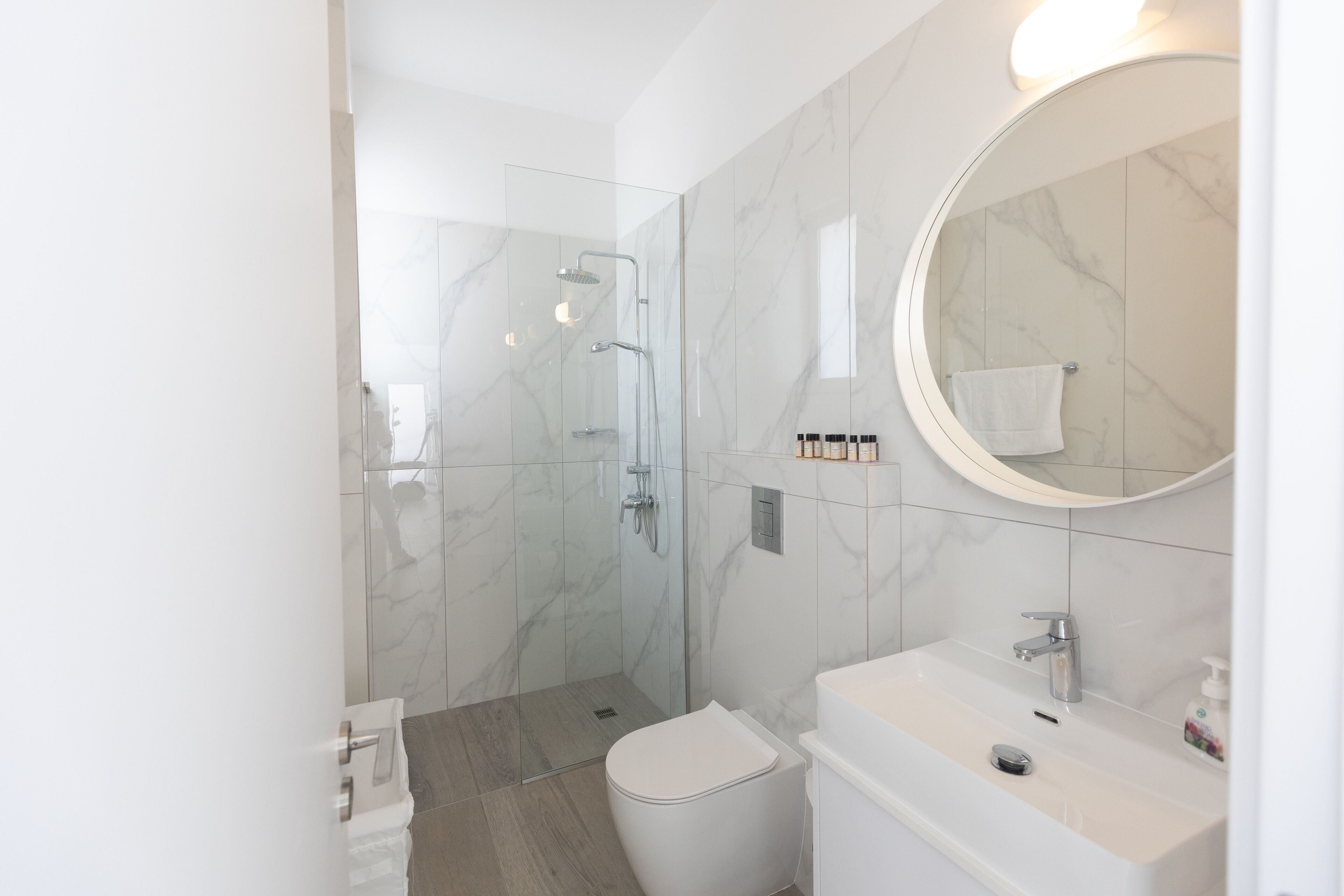 A modern bathroom with a glass-enclosed shower, a white toilet, and a sink with a mirror above it.