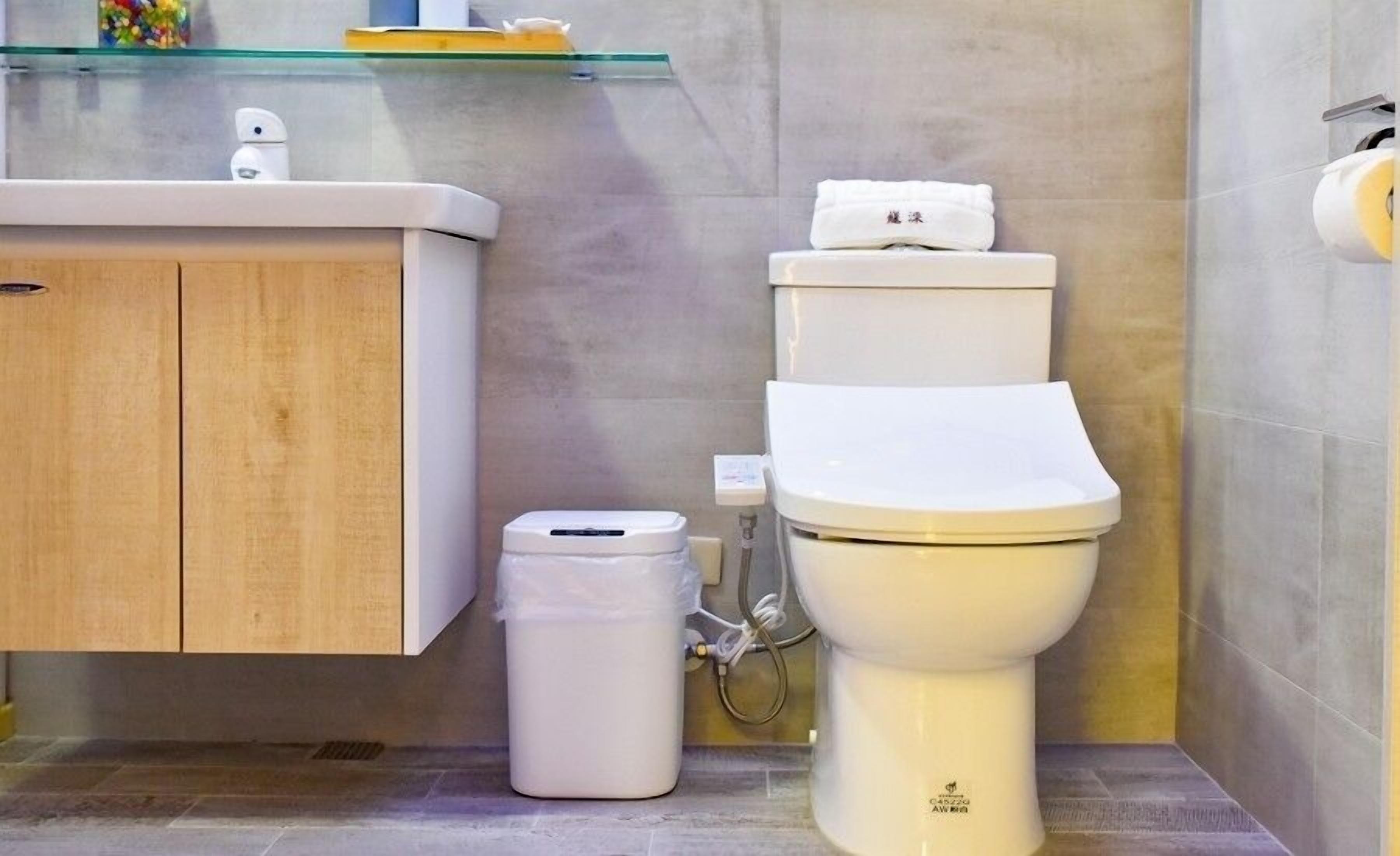 Ein modernes Badezimmer mit Toilette, einem Mülleimer und einem Ablagefach aus Glas über dem Waschbecken.