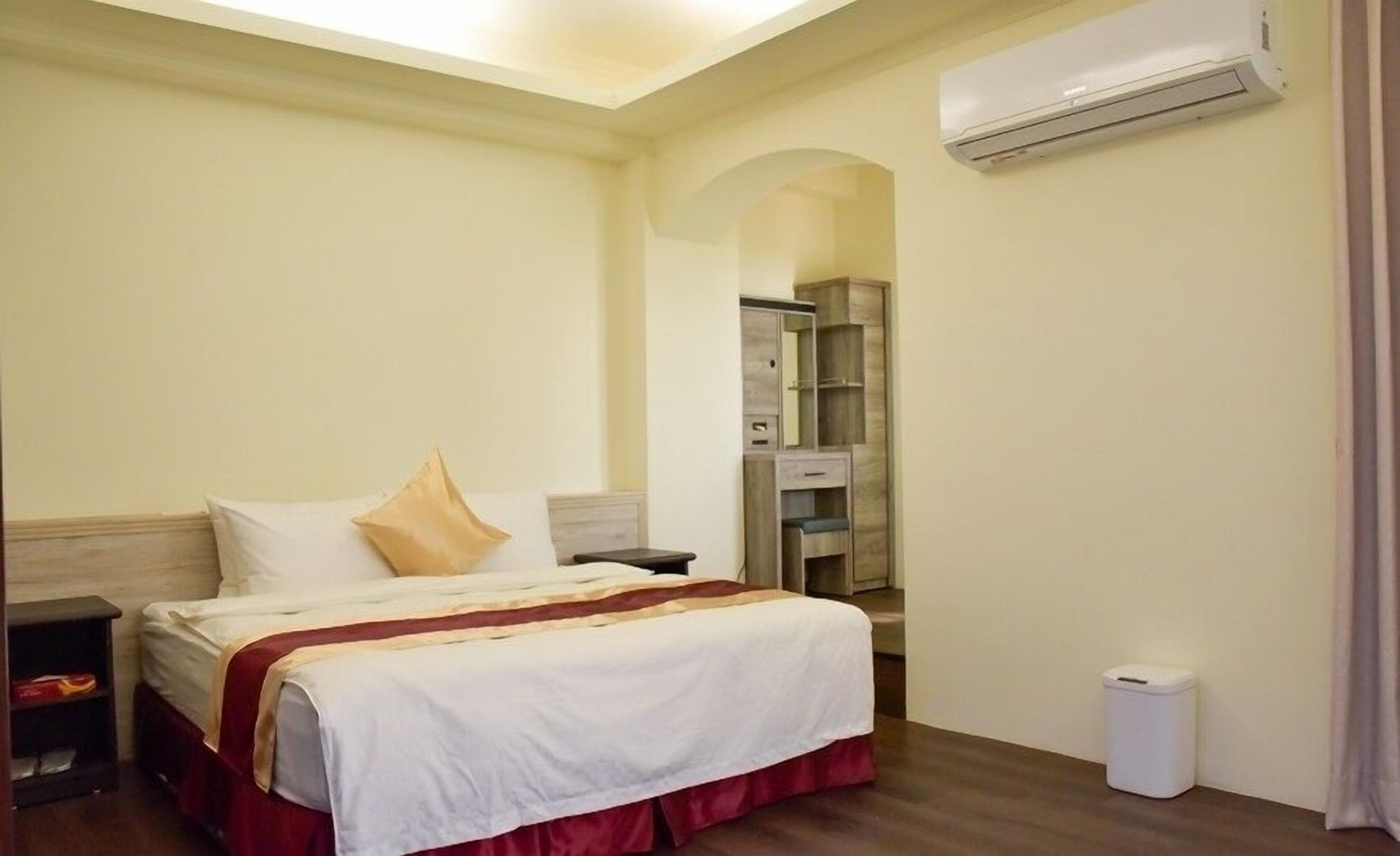 Ein Hotelzimmer mit einem Bett, Nachttischen, einem Kleiderschrank und einer Klimaanlage.