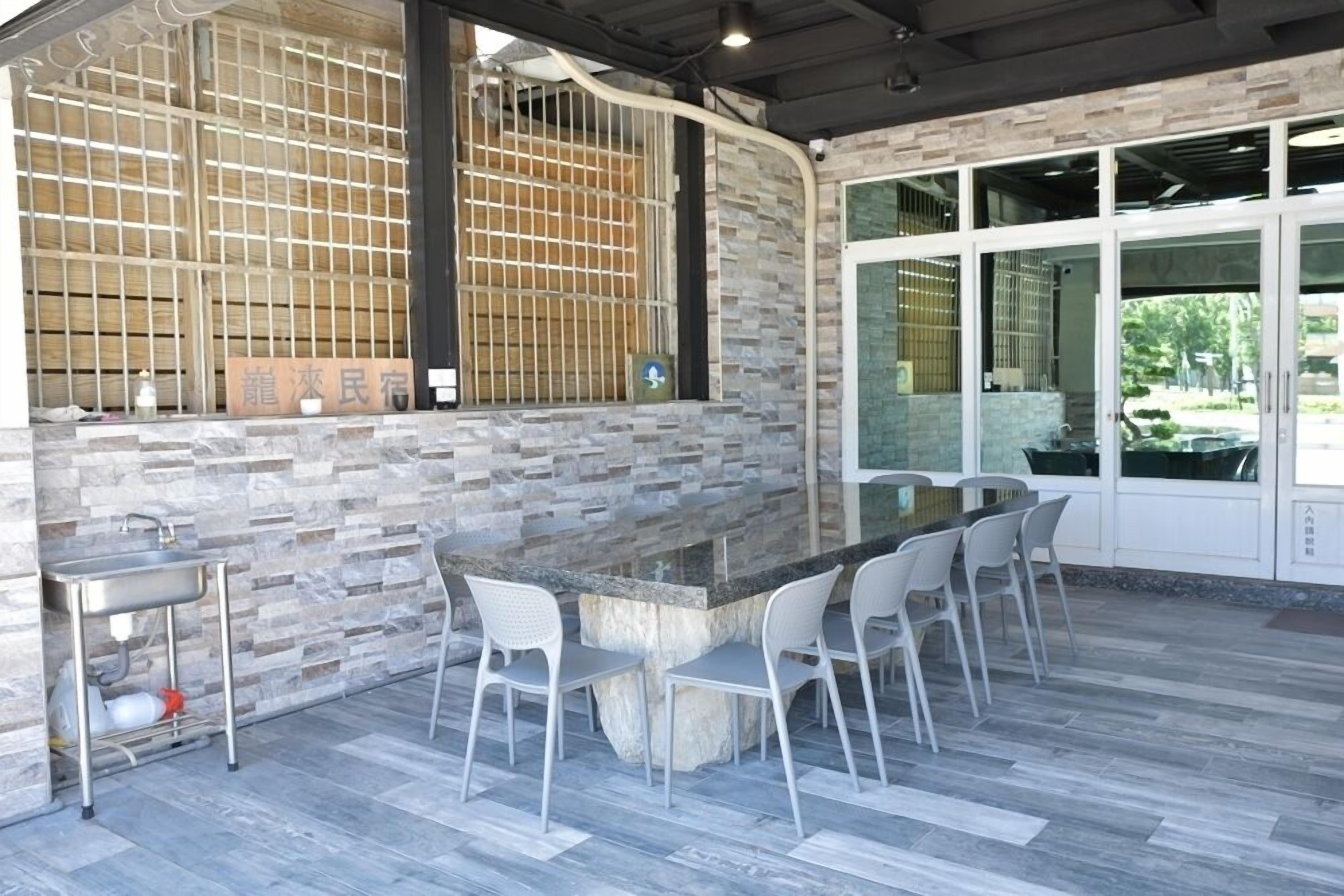 An outdoor bar area with a stone countertop, white chairs, and a stone wall with a grid pattern.