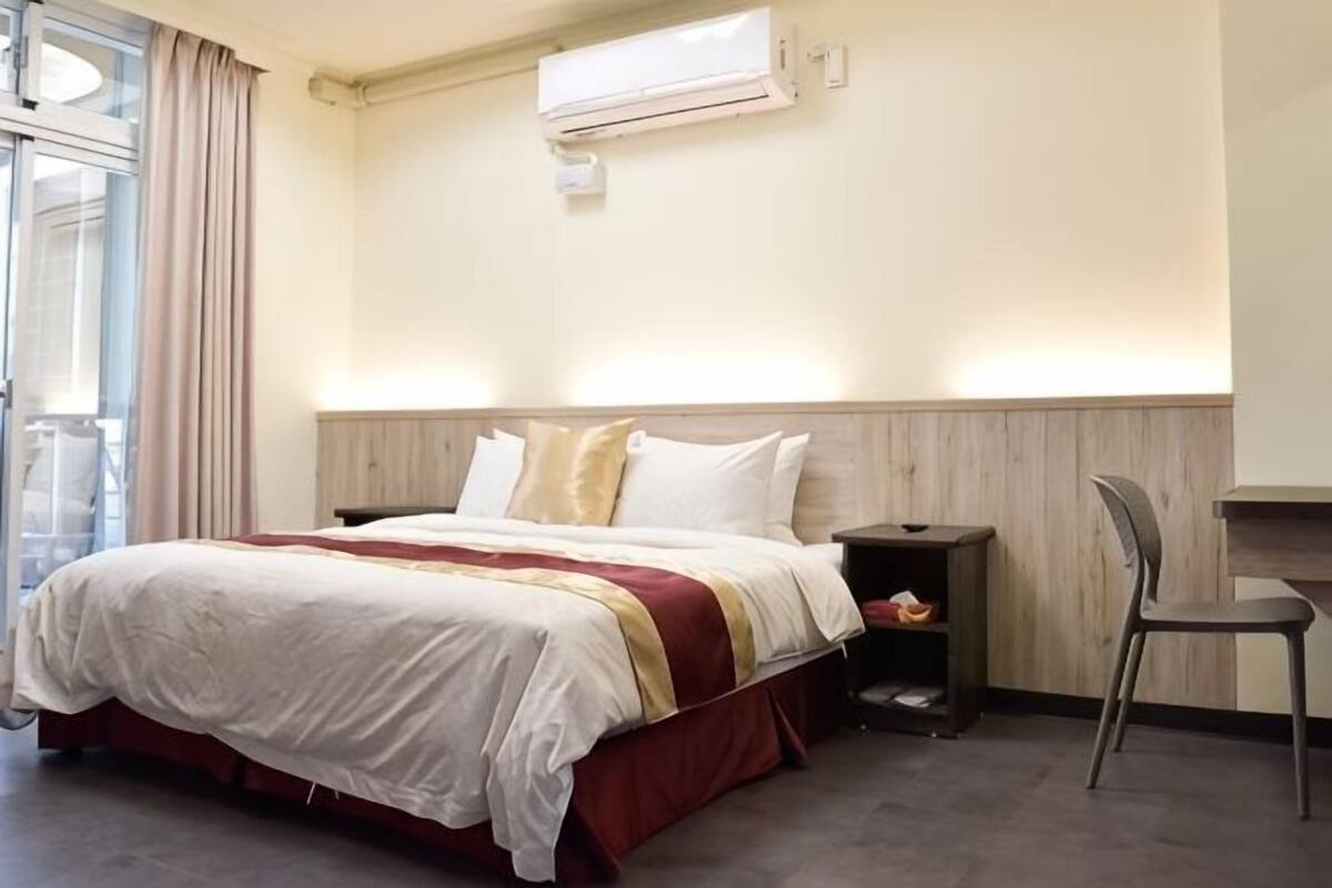 A hotel room with a bed, a chair, a desk, and a window with curtains.