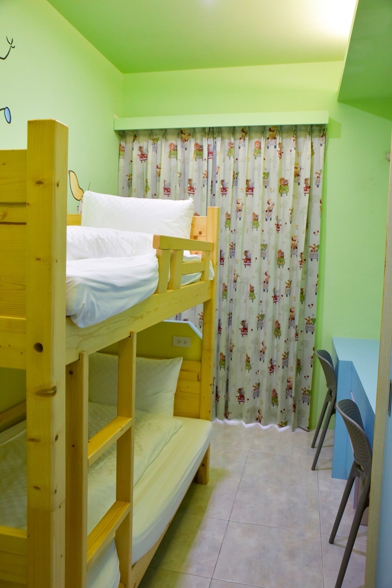 Une chambre avec un lit superposé, un bureau et une chaise, un rideau à motifs et un mur vert.