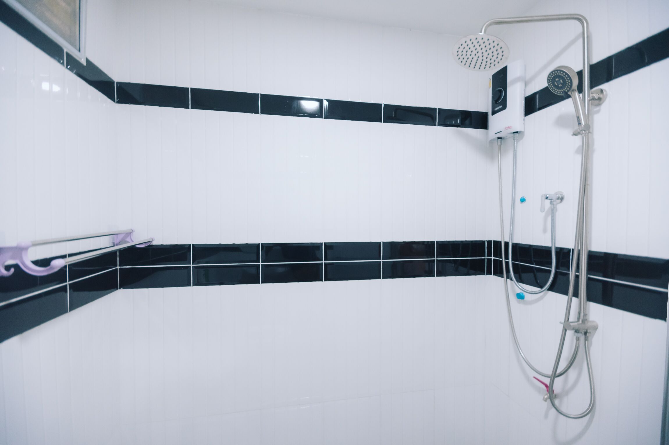 Ein Badezimmer mit weiß gefliesten Wänden, einer Wand mit schwarz-weißen Streifen als Blickfang, einer Dusche mit Duschhandstück und einem Handtuchhalter mit einem violetten Handtuch.