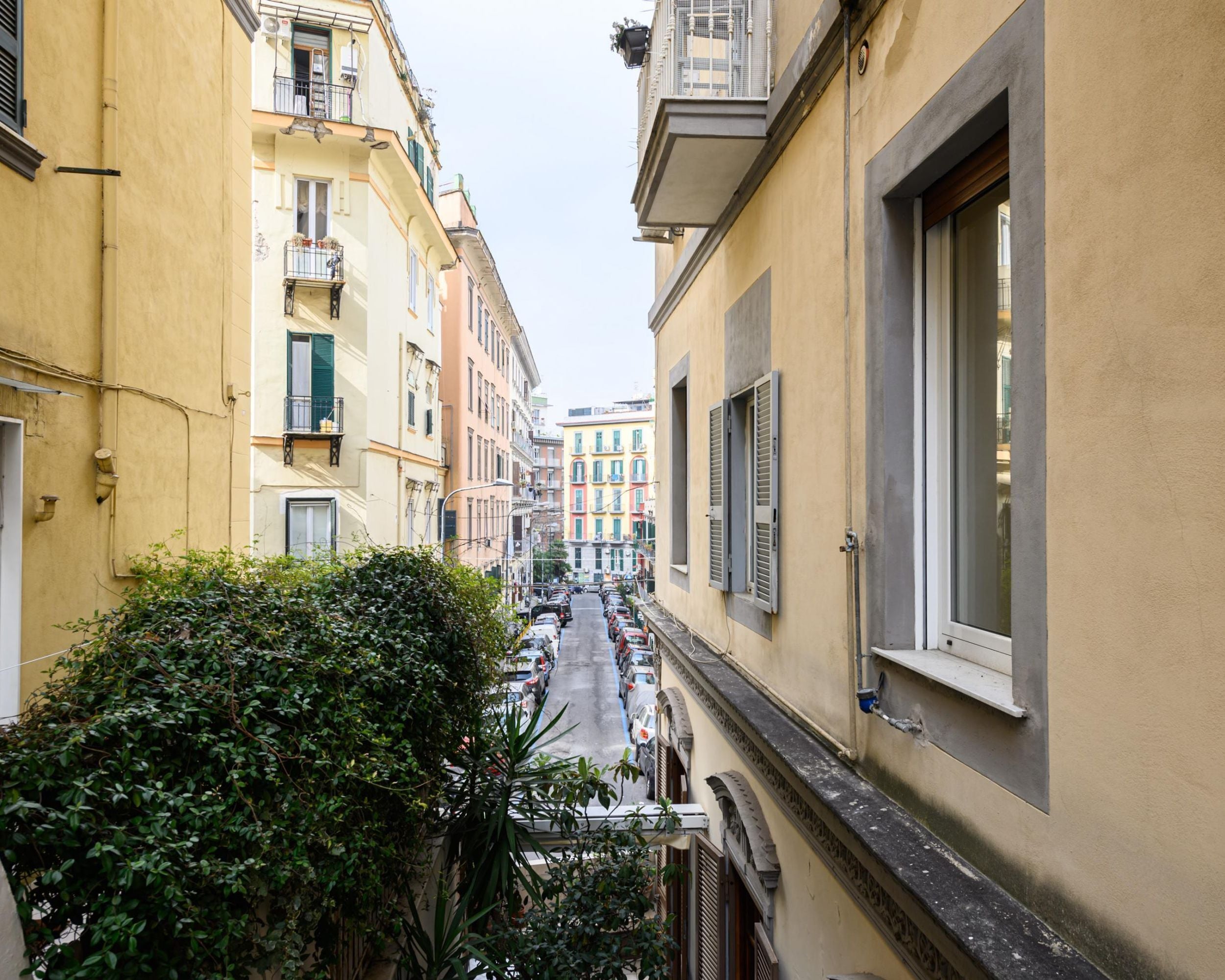 A narrow street with buildings on either side, featuring balconies and shutters.