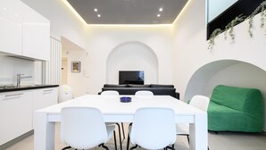 A modern kitchen with white cabinets, a dining table with chairs, a black sofa, and a green armchair.