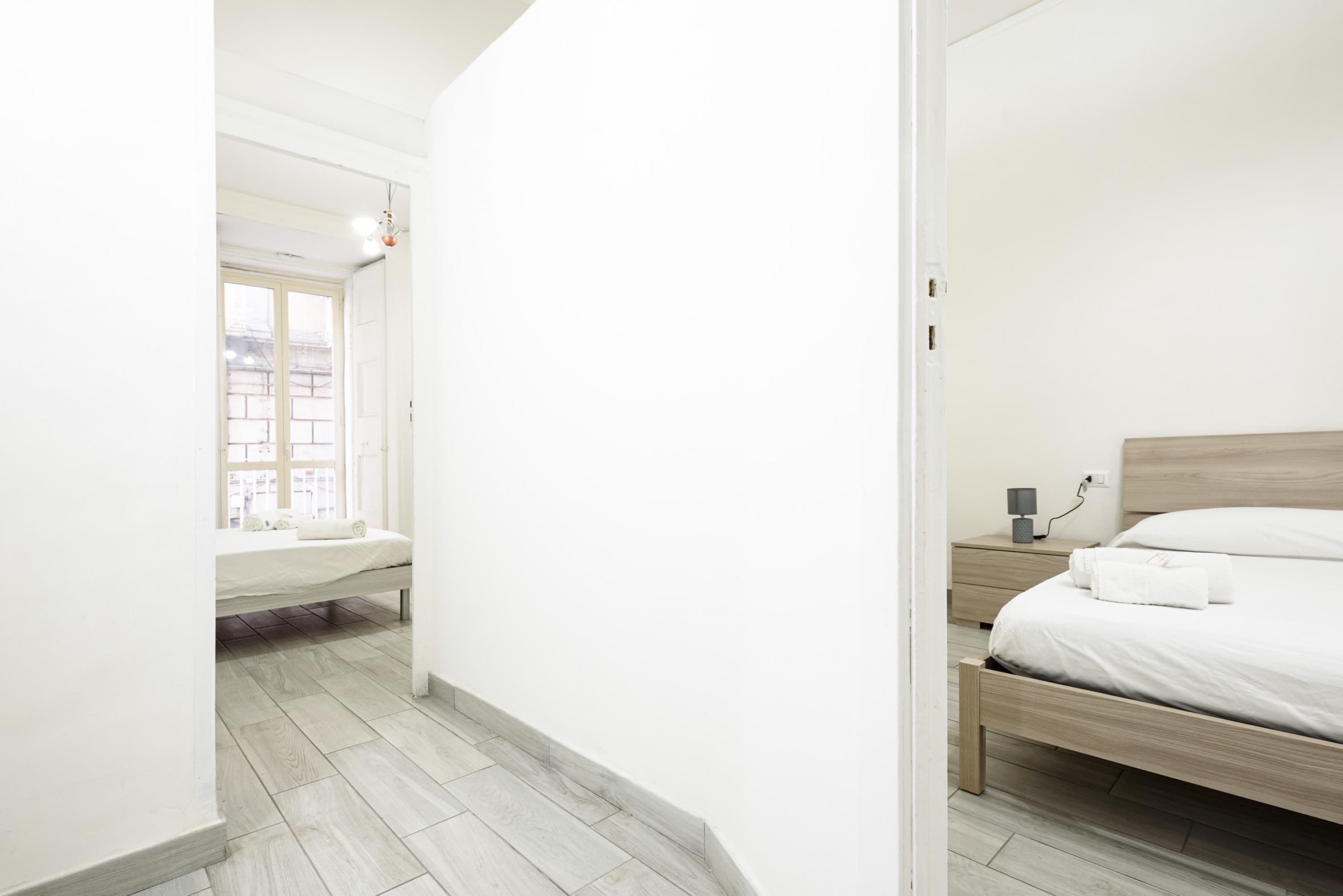 A minimalist bedroom with a wooden bed, a bedside table, and a window with a view of buildings.