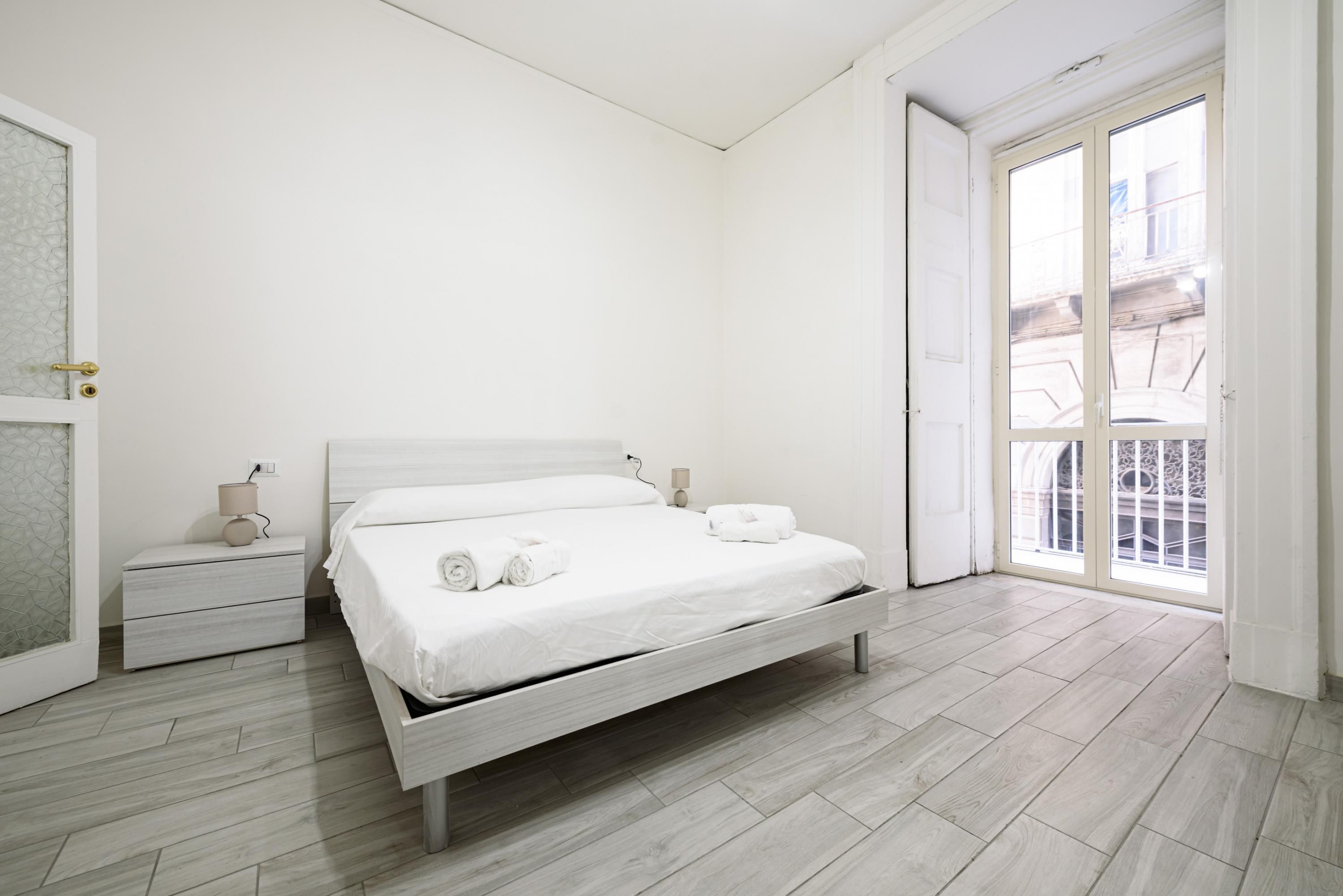 Un dormitorio minimalista con cama, mesita de noche y vistas a través de un ventanal corredero.