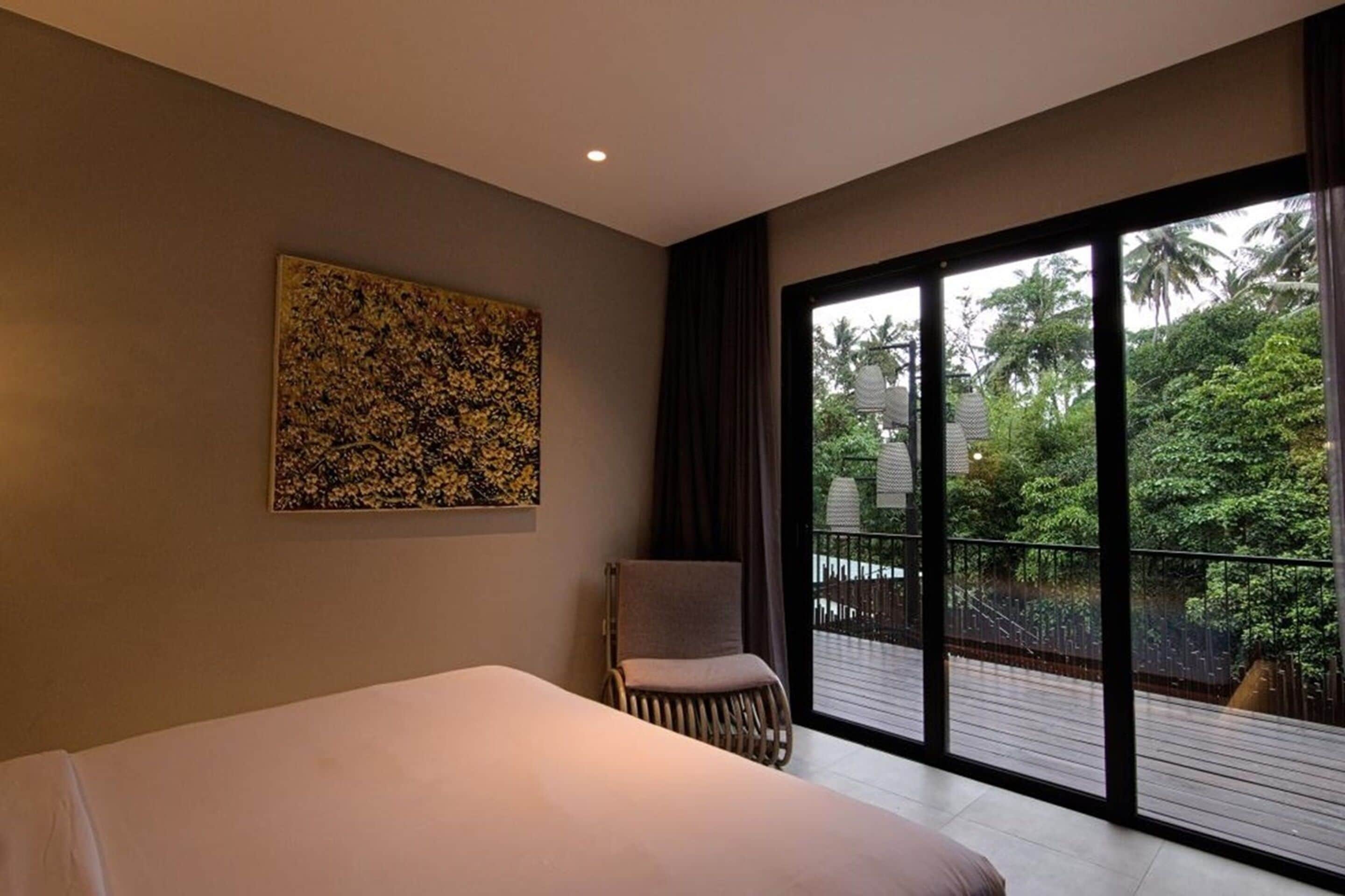 Une chambre avec un grand lit, une chaise, une fenêtre et un tableau accroché au mur.