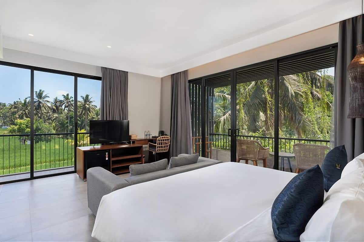 A modern hotel room with a large bed, a TV, and a balcony with a view of palm trees.