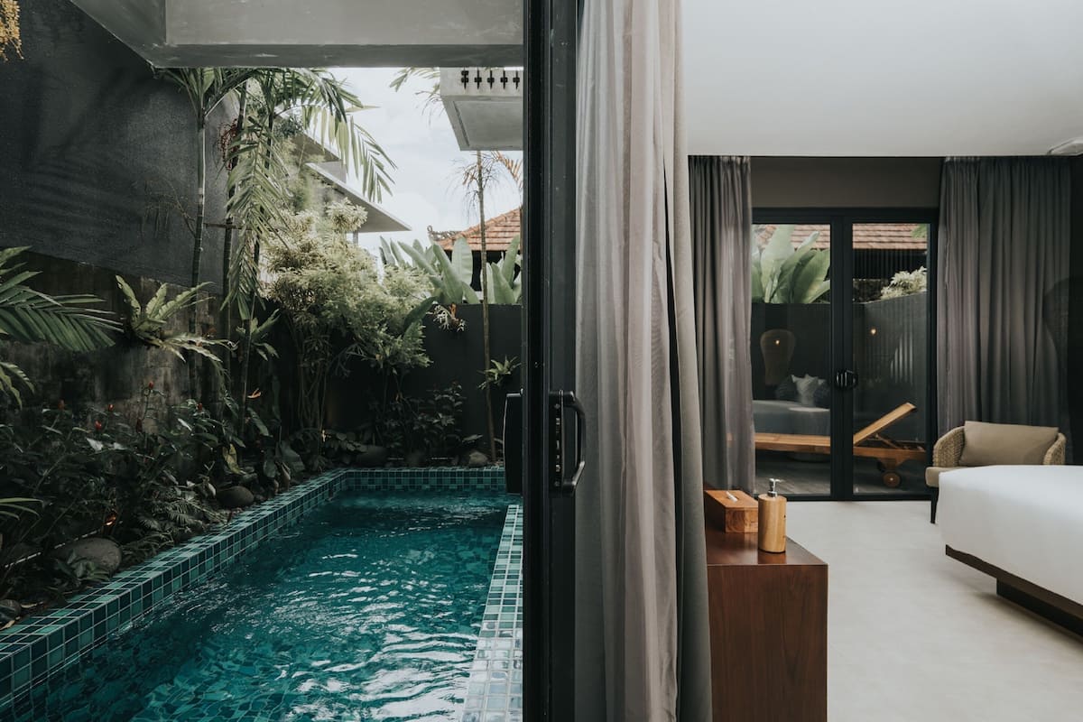 A modern hotel room with a private pool, a balcony with plants, and a view of the outside.