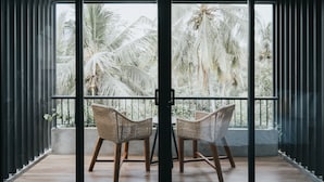 Un balcón con dos sillas de mimbre y una mesa, con vistas a palmeras.