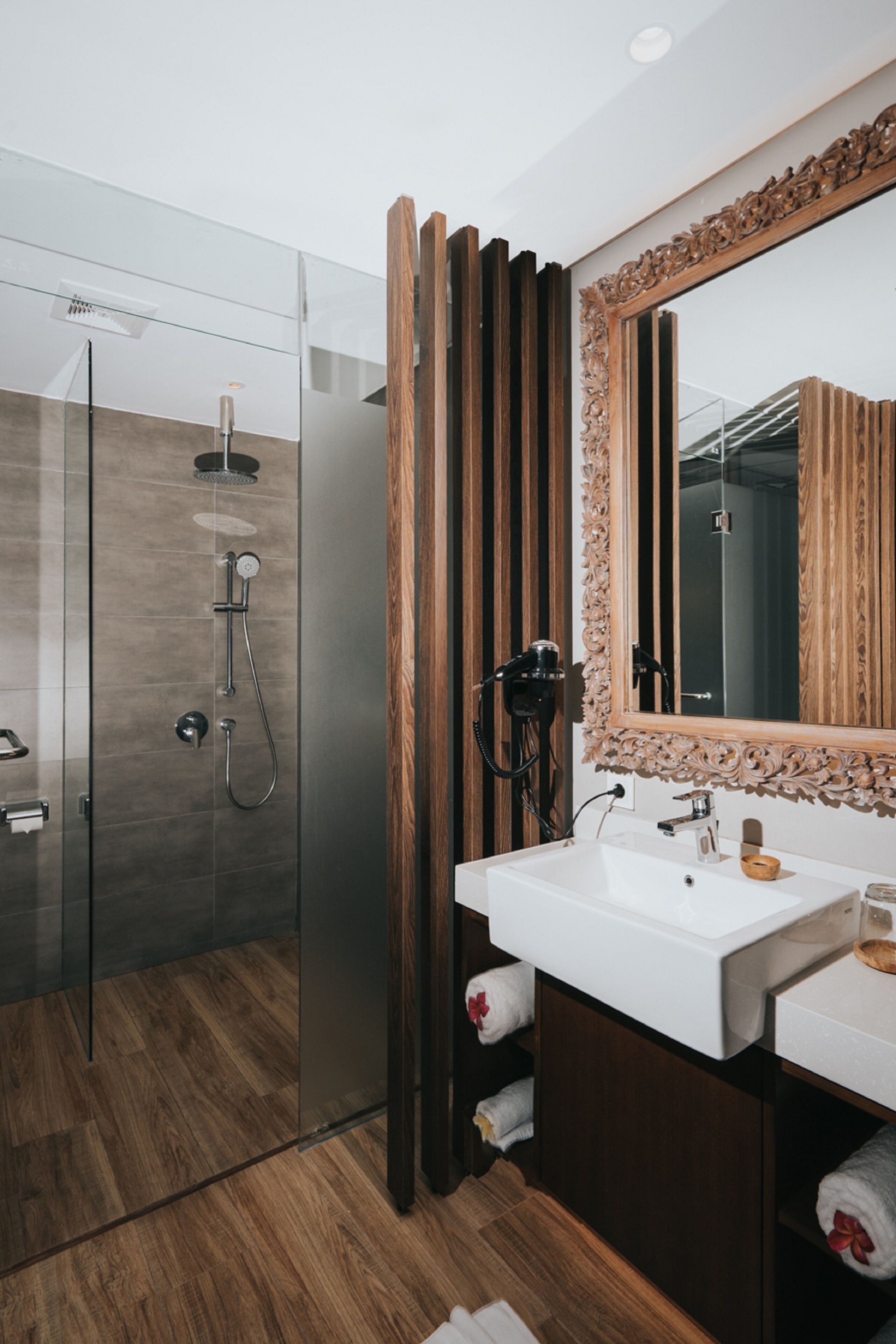 A modern bathroom with a glass shower enclosure, a wooden vanity, and a large mirror with an ornate frame.