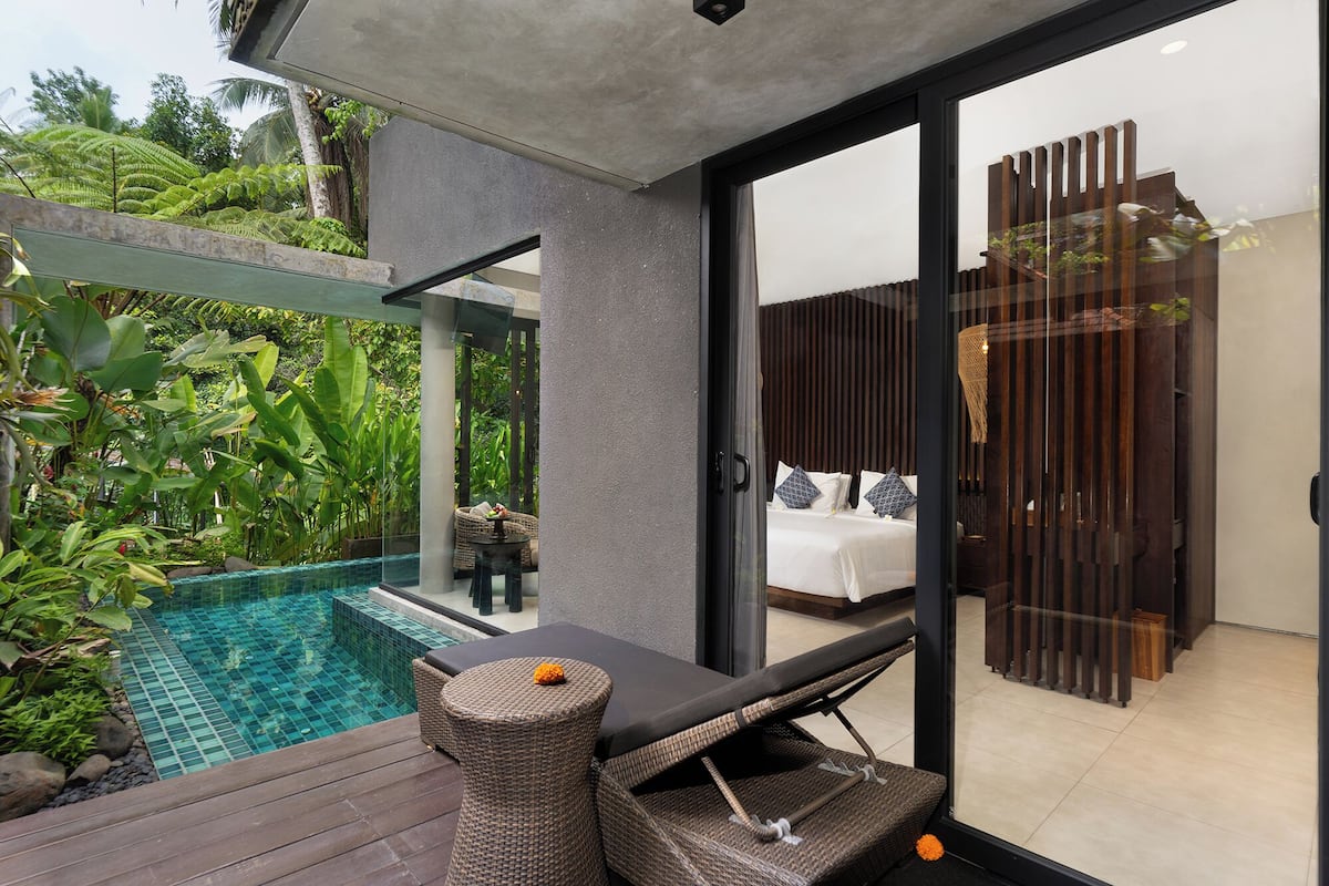 A modern outdoor pool area with a lounge chair and a small table, surrounded by lush greenery.