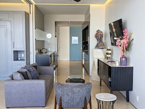 Uma sala de estar moderna com um sofá cinza, uma mesinha redonda e uma TV sobre um armário preto.