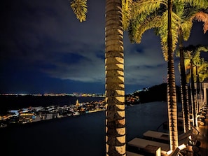 Vista costeira noturna com palmeiras, marina e edifícios iluminados.
