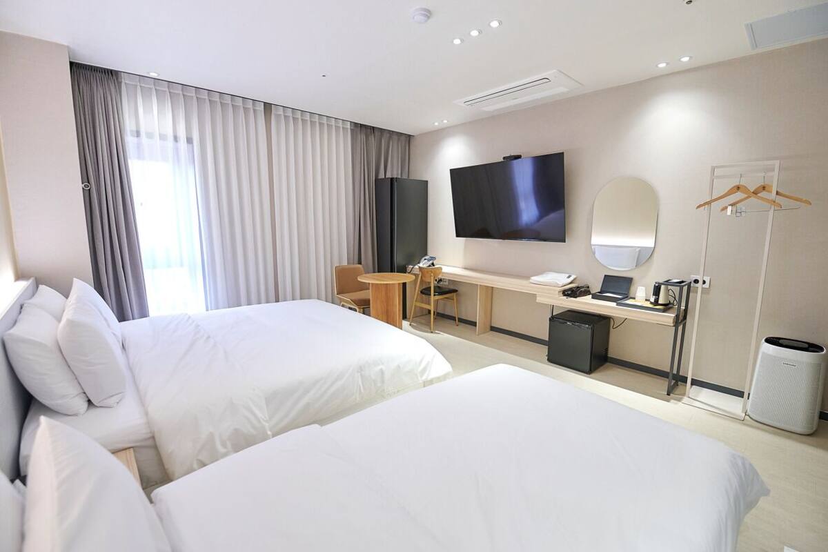 A hotel room with two beds, a desk with a laptop, a TV, a mirror, and a wardrobe.