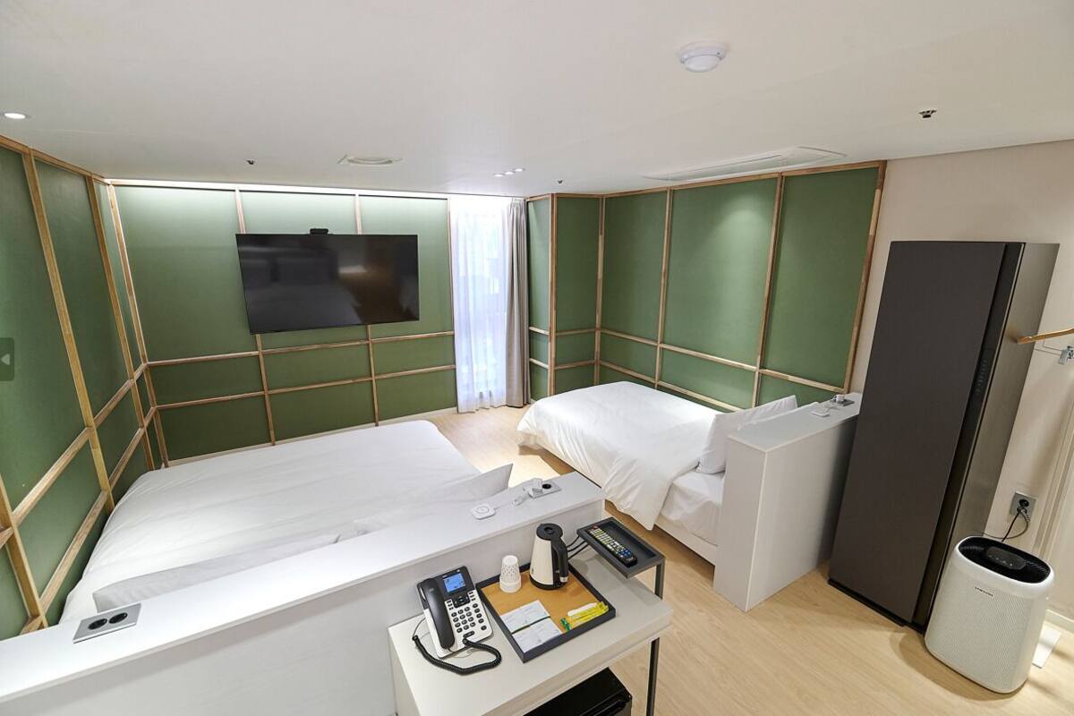 A hotel room with a single bed, a desk with a telephone and a notepad, a mirror, a wardrobe, and a television on the wall.