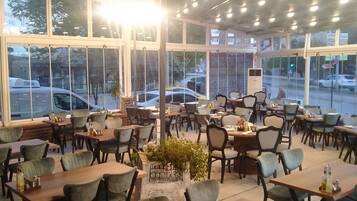 An indoor dining area with multiple tables and chairs, large windows, and a central decorative planter.