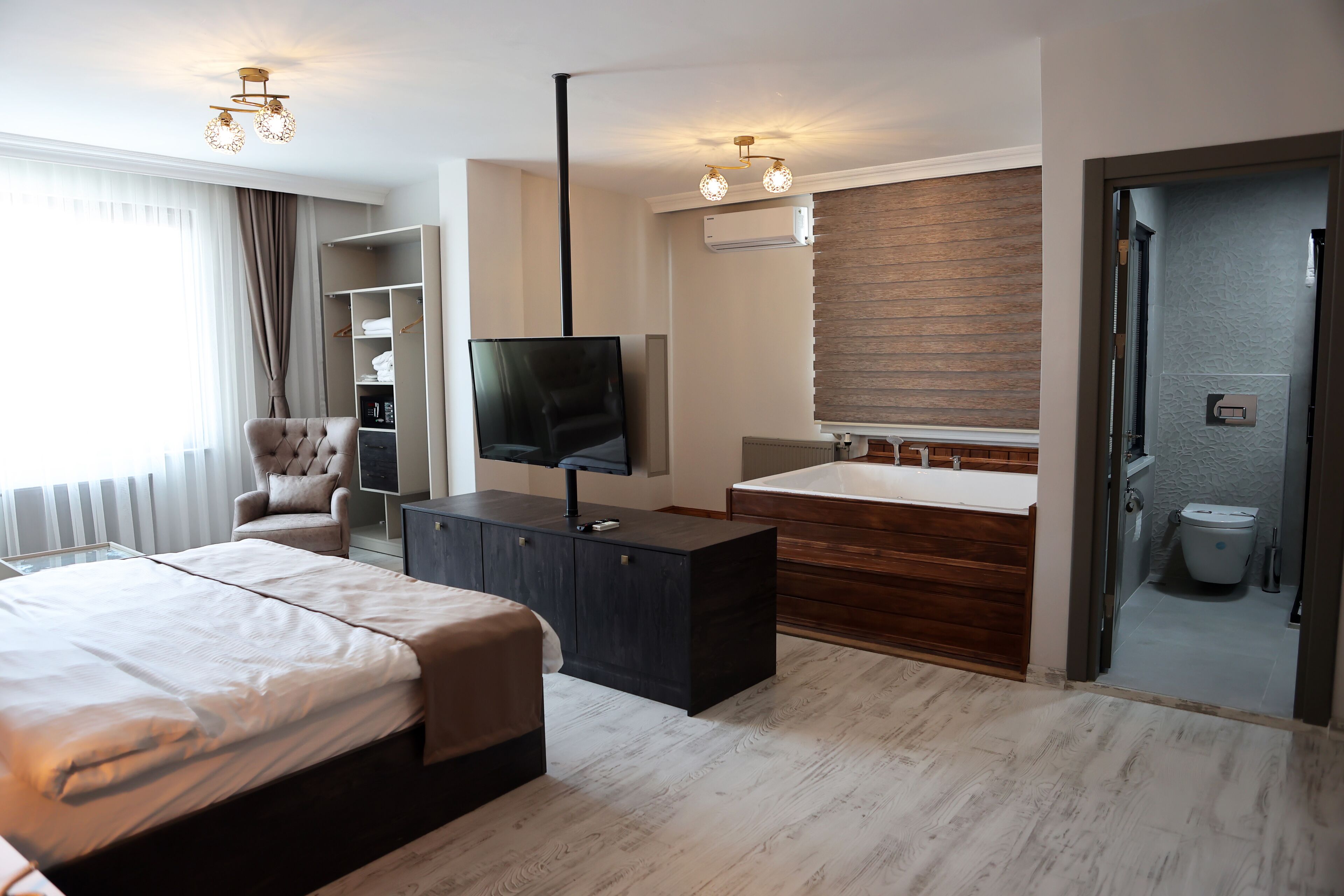 Quarto de hotel moderno com uma cama grande, televisão, escrivaninha e banheiro visível por uma porta aberta.