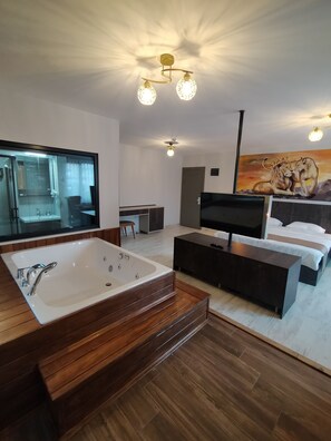 Ein modernes Schlafzimmer mit einem großen Bett, einem Fernseher, einem Schreibtisch und einem Badezimmer mit einer Badewanne.