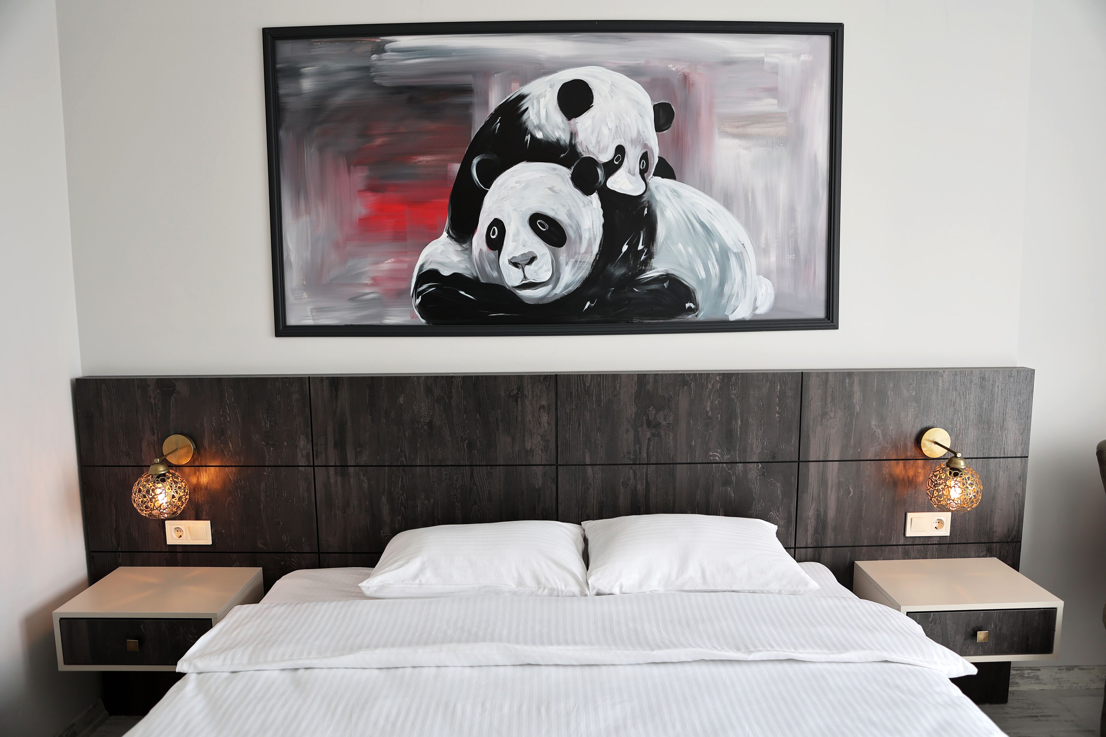 A bedroom with a large bed, two bedside tables with lamps, and a framed painting of pandas on the wall.