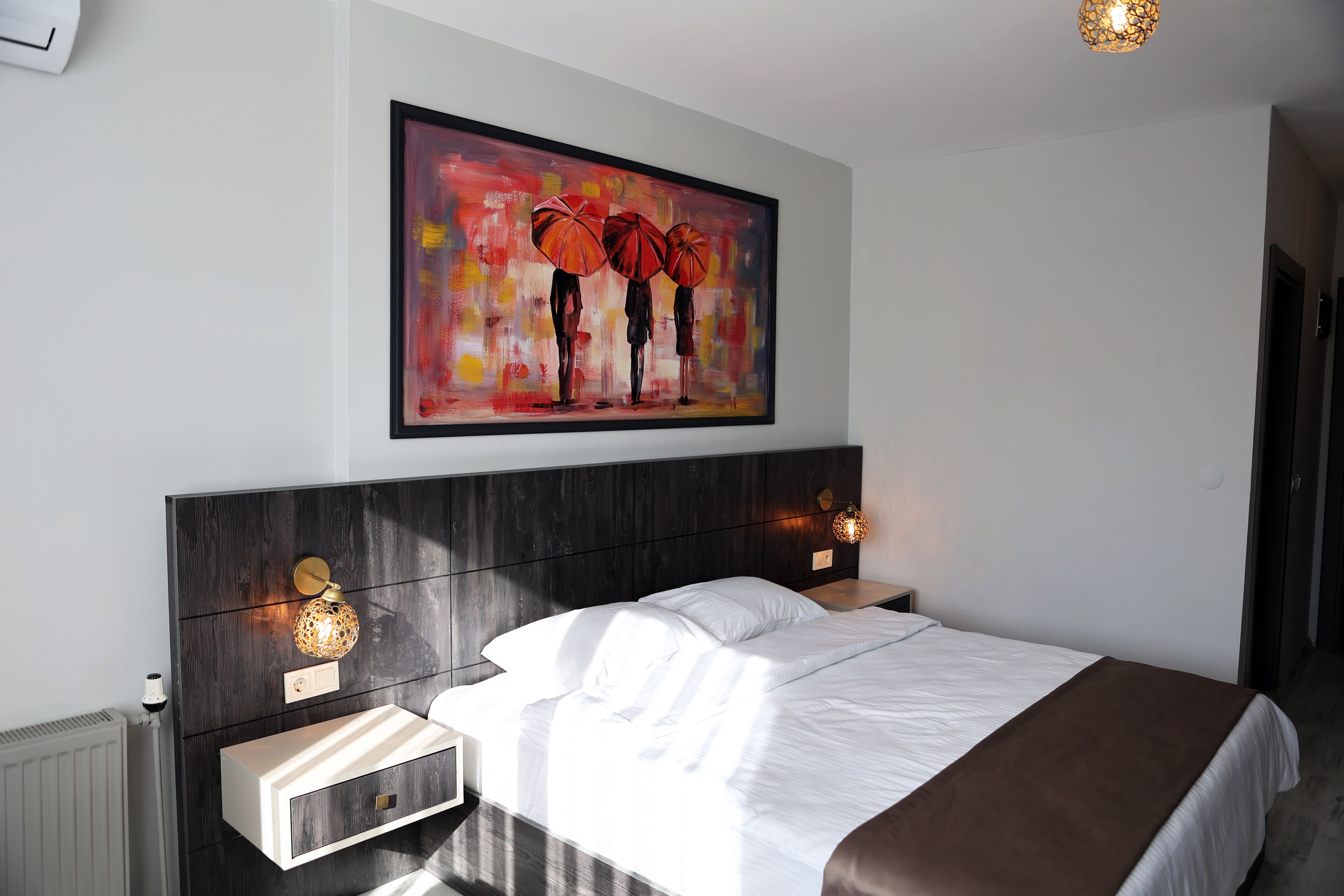 Una habitación de hotel moderna con una cama grande, mesitas de noche, una obra de arte enmarcada y una lámpara de pared.