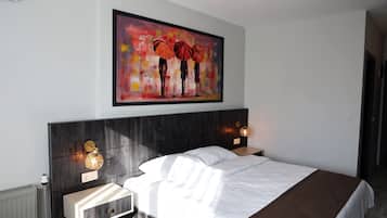 Una habitación de hotel moderna con una cama grande, mesitas de noche, una obra de arte enmarcada y una lámpara de pared.