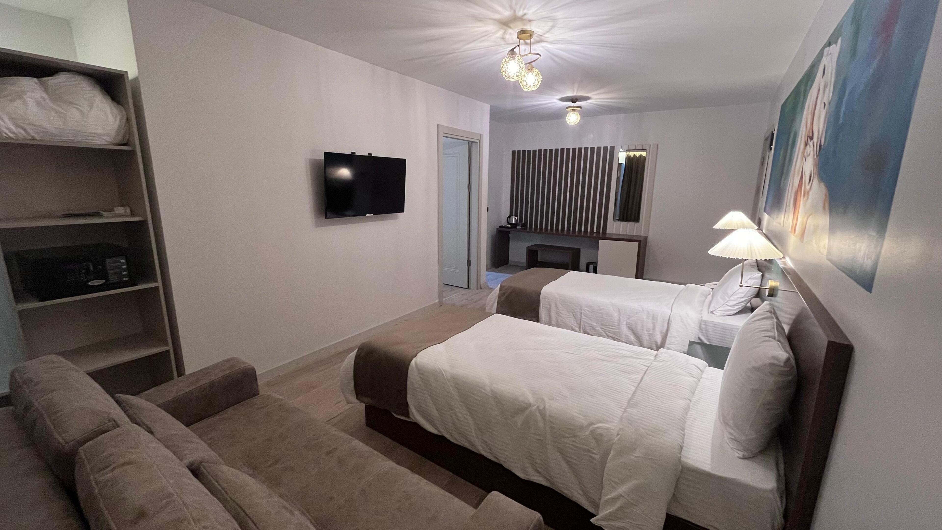 A hotel room with two beds, a TV, a bookshelf, a sofa, a fireplace, and a painting on the wall.