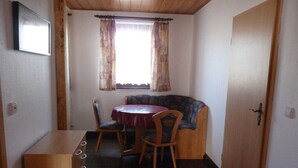 Une pièce de taille modeste comprenant une table et des chaises, un canapé, un meuble en bois et une fenêtre avec des rideaux.