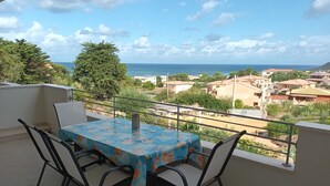 Un balcon avec une table et des chaises, donnant sur une ville côtière avec ses bâtiments et ses arbres.