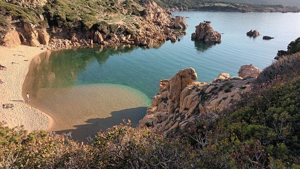 Un paysage côtier caractérisé par des falaises rocheuses, des eaux cristallines et une plage de sable.