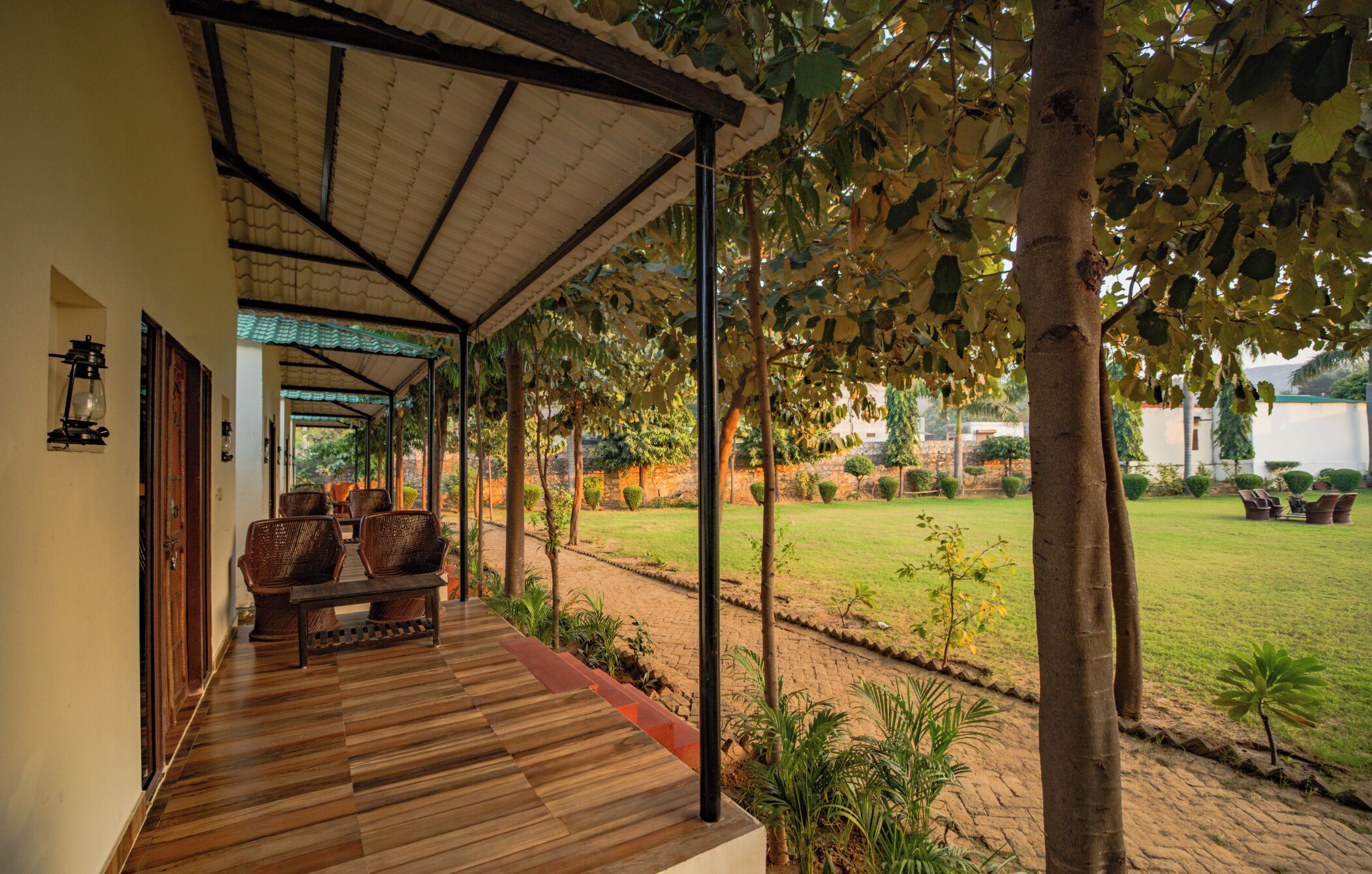 Varanda coberta com piso de madeira, móveis de vime e vista para um jardim e gramado bem cuidados.