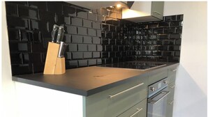 A modern kitchen with black tiled backsplash, a black countertop, and green cabinets. - Sumptuous Beau-Rivage apartment with lake view and private beach (Annecy)