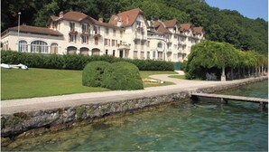 A large, multi-story hotel with a symmetrical facade, a manicured lawn, and a body of water in front. - Sumptuous Beau-Rivage apartment with lake view and private beach (Annecy)