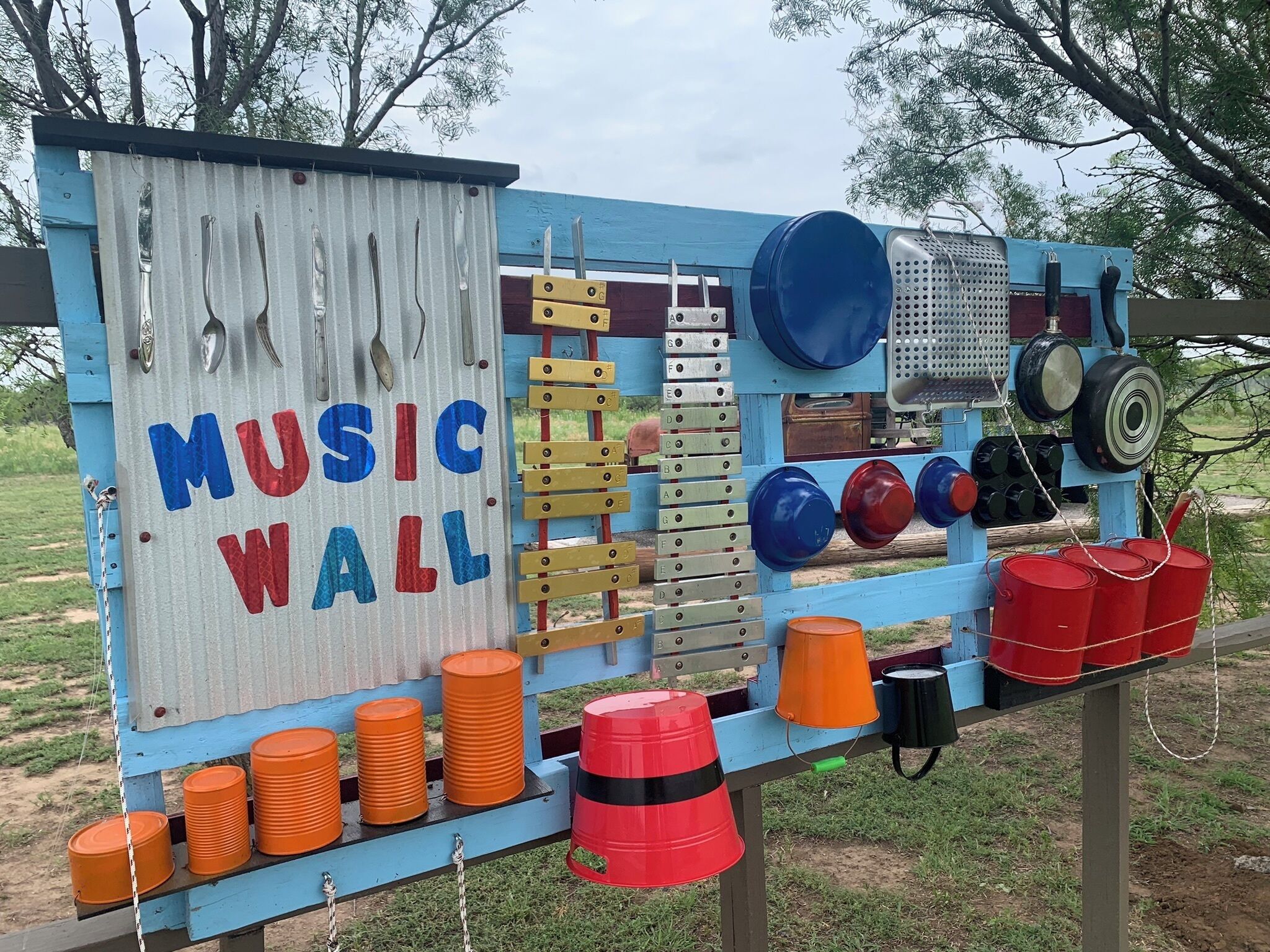 A blue and white structure labeled "MUSIC WALL" with various musical instruments and storage bins.