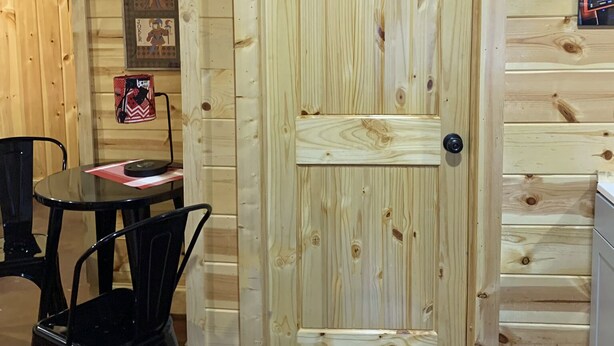 Un intérieur en bois avec une porte, une table entourée de chaises et un tableau encadré accroché au mur.