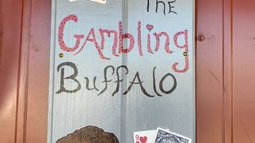 Una puerta de madera con el texto "The Gambling Buffalo" e ilustraciones de cartas de juego y un búfalo.