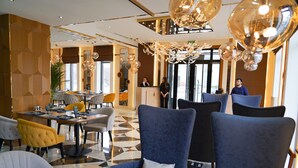 Un hall d’hôtel moderne avec un motif géométrique sur le sol, un comptoir d’accueil et des espaces détente avec des chaises bleues et jaunes.