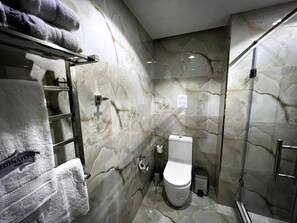 A bathroom with a marble wall, a toilet, a glass shower enclosure, and a towel rack with towels. - MedinaTown (Tashkent)