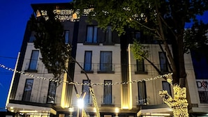 Un hôtel à plusieurs étages, doté d’une façade moderne, d’un tapis rouge à l’entrée et de guirlandes lumineuses décorant l’extérieur.