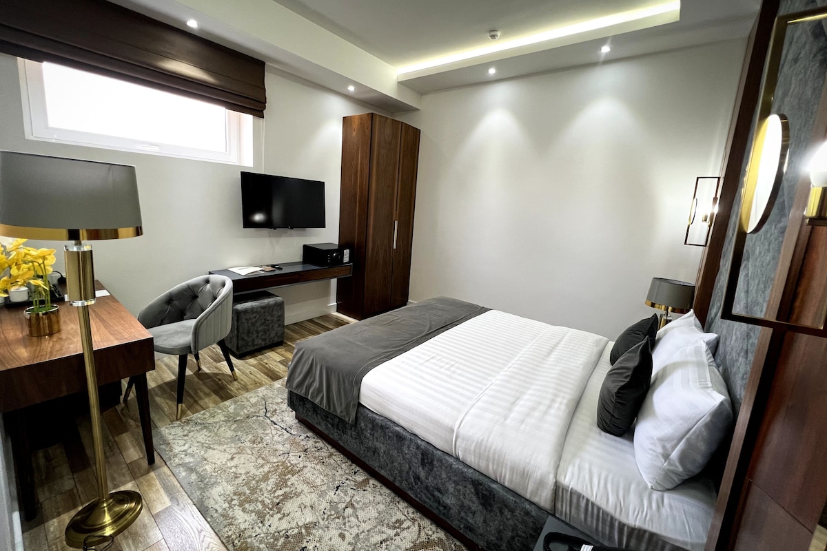 A modern hotel room with a bed, desk, chair, television, and a large window.