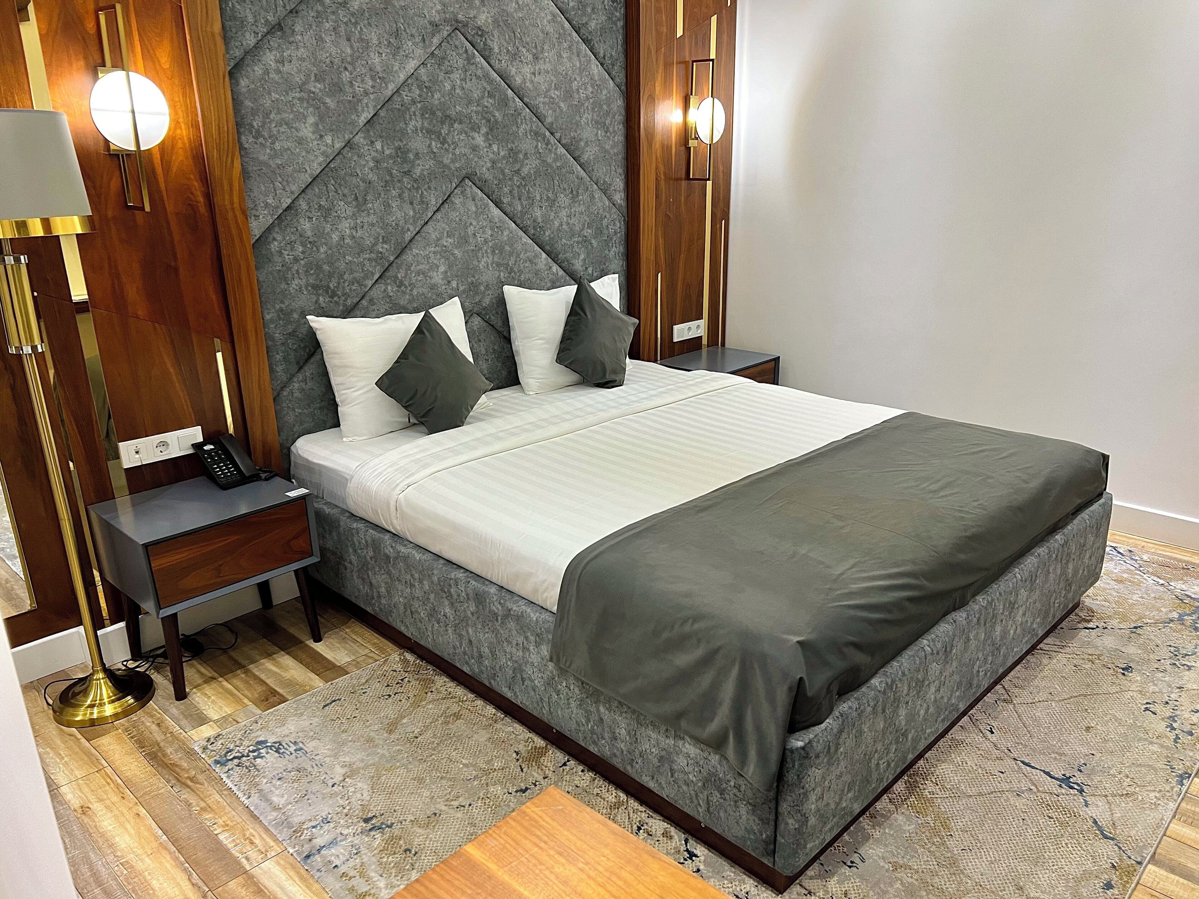 A modern bedroom with a large bed, a bedside table with a phone, and a nightstand with a lamp.