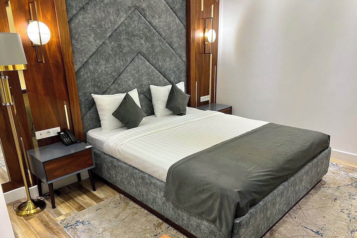 A modern bedroom with a large bed, a bedside table with a phone, and a nightstand with a lamp.